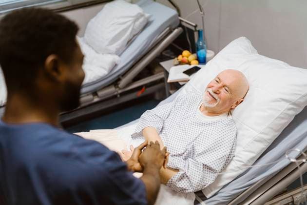 Male nurse holding hands of smiling senior patient lying on bed in hospital Germany, Berlin, model released, property released Copyright: xMaskotx , MA100146 MA100146