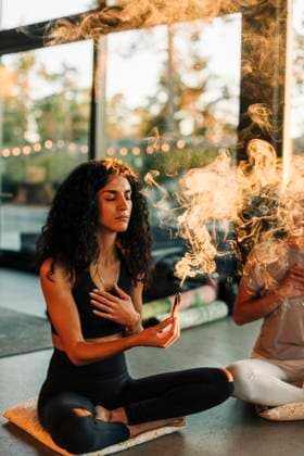 Woman with hand on chest holding burning sandalwood while sitting cross-legged at retreat center Sweden, Stockholm, model released, property released Copyright: xMaskotx , MA100444 MA100444