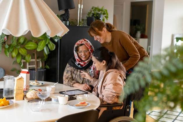 Female caregiver talking to woman with paraplegia and her mother sitting at dining table in home Sweden, Stockholm, model released, property released Copyright: xMaskotx , MA99996 MA99996