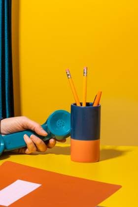Plastic blue handset of stationary telephone placed near pencils and notebook on table during phone call against yellow background Rodobot_ID13176_401967_021 Copyright: xRodobotx Model Released
