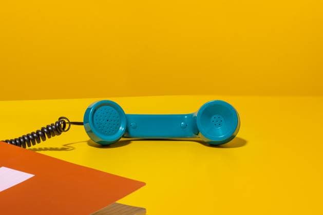 Plastic blue handset of stationary telephone placed near notebook on table during phone call against yellow background Rodobot_ID13176_401976_027 Copyright: xRodobotx Model Released