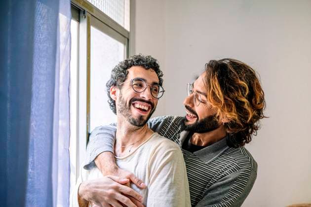 Happy gay man with arm around boyfriend near window at home model released, Symbolfoto property released, GDBF00054