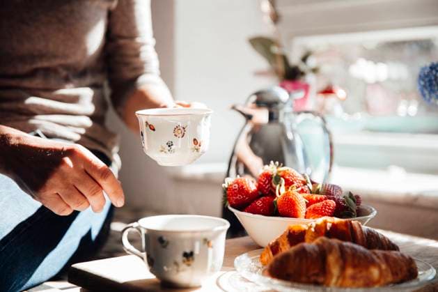 Woman holding coffee cup with croissant and fresh strawberries in kitchen model released, Symbolfoto property released, JOSEF18226