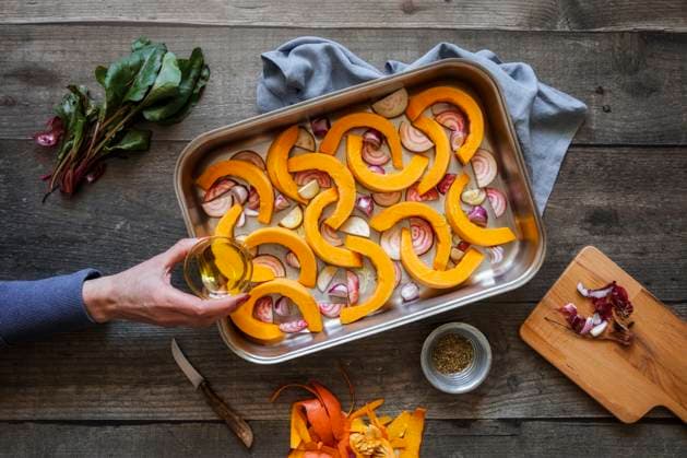 Hand of woman sprinkling olive oil on sliced onions, pumpkins and common beets on baking sheet model released, Symbolfoto, EVGF04319
