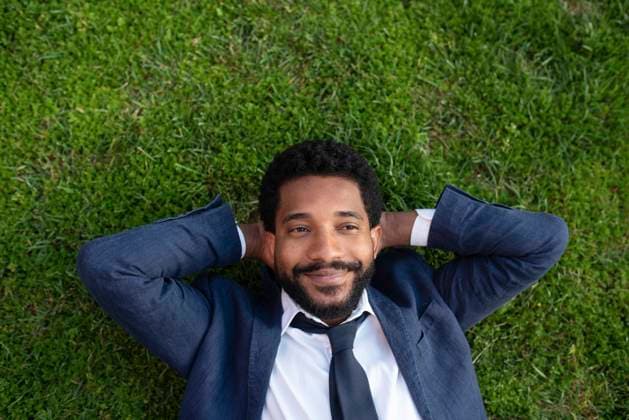 Thoughtful smiling businessman with hands behind head lying on grass model released, Symbolfoto, VRAF00099