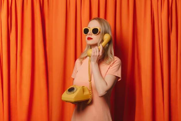 Woman wearing sunglasses talking over landline phone in front of orange curtains model released, Symbolfoto, VSNF00685