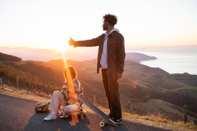 RECORD DATE NOT STATED MR_ID12975_13172_IbaiMovilla.jpg, MR_ID12975_13173_HannahWurzinger.jpg Side view of young black man with skateboard showing thumb up gesture while standing near girlfriend in mountains on sunset, Model released IoritzLopez_ID12975_394770_034 Copyright: xIoritzxLopezx MR