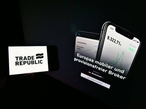 Person holding mobile phone with logo of German online broker Trade Republic Bank GmbH on screen in front of web page. Focus on cellphone display. *** Person haltend Mobiles Telefon mit Schriftzug des Deutsche Onlinerechnung Makler Handel Republik bank¡ GmbH&Co am Bildschirm ÊIn vorne des Webs Seite Fokus am cellphone Anzeige 3034877