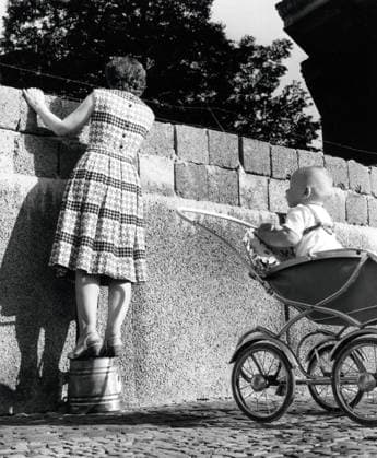 Eine junge Mutter schaut über die Mauer Eine junge Mutter, dahinter ihr Kind in seinem Kinderwagen, schaut über die Mauer in der Bernauer Strasse in den Ostsektor von Berlin, Deutschland 1961., Berlin Copyright: Kindermann Nur redaktionelle Nutzung. Editorial usage only. KIN_7402001005 EDITORIAL USE ONLY