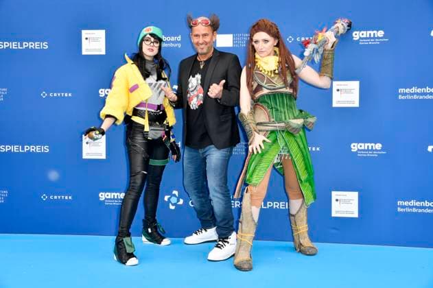 Tom Lehel mit den Cosplayern Killjoy und Aloy bei der Verleihung des Deutschen Computerspielpreises 2023 im Spindler & Klatt. Berlin, 11.05.2023