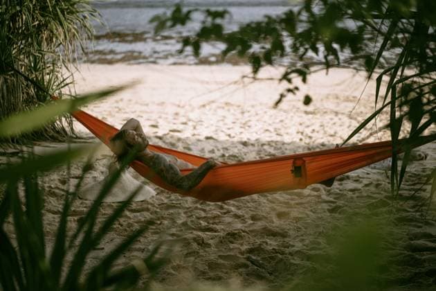 A young man rests and chills in an orange hammock on the beach n Nusa Penida, Bali, Indonesia CR_YUKI230221-1130717-01 ,model released, Symbolfoto ,property released