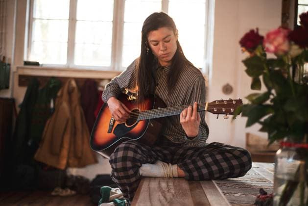 Asian person sits at home on wooden table playing guitar CR_PIDODS230510-1038926-01 ,model released, Symbolfoto