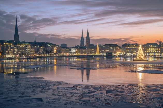 Germany, Hamburg, Ice floating in Alster Lake at dusk with city skyline and glowing Christmas trees in background, KEBF02715