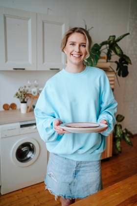 Smiling young woman holding plates standing in kitchen at home model released, Symbolfoto property released, MDOF01053