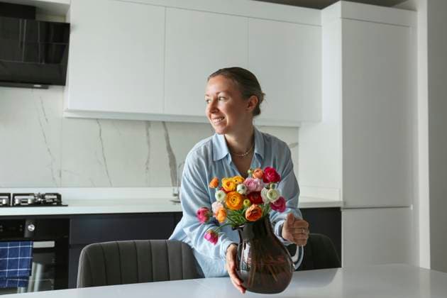 Smiling woman keeping Ranunculus vase on table in kitchen at home model released, Symbolfoto property released, SYEF00389
