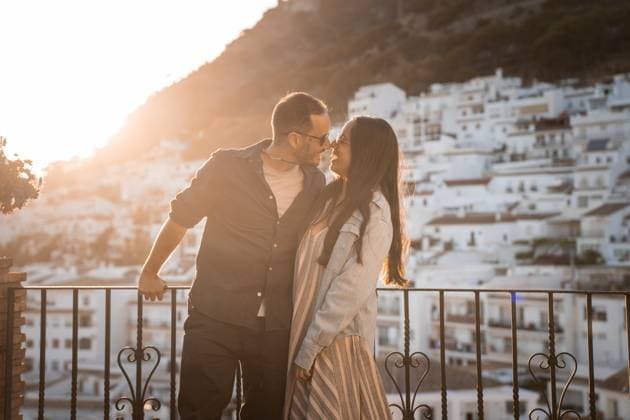 IMAGO Creative, Urban Lifestyle Loving couple standing close on balcony Happy couple in sunglasses hugging smiling on balcony with fence while looking at each other against city buildings and mountain during sunset time PabloMenendez_ID14105_425562_040 Copyright: xPabloxMenendezx Model Released