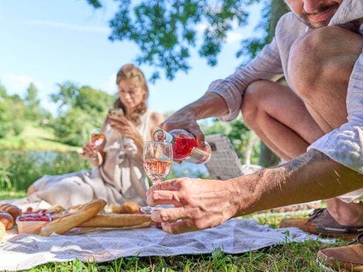 A man pouring wine into the glass with a female in the background picnicking in the park *** einer Mann einschenkend Wein hinein der Glas mit einer weiblich ÊIn der Hintergrund picnicking ÊIn der parkähnliche 9825328 ,model released, Symbolfoto RECORD DATE NOT STATED