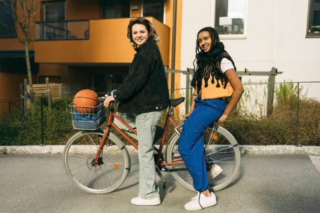 Portrait of smiling female friends sitting on bicycle in front of building at footpath Sweden, Stockholm, model released Copyright: xMaskotx , MA101965 MA101965