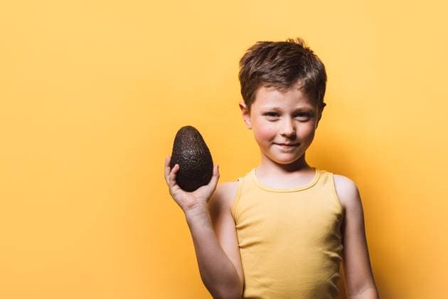 Happy boy in casual outfit smiling while holding and looking at tasty ripe fresh avocado and standing looking at camera on yellow background in studio HodeiUnzueta_ID15006_458359_002 Copyright: xHodeixUnzuetax RECORD DATE NOT STATED Model Released