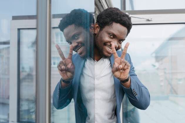 Creative Highlights Symbolbilder Smiling businessman showing peace sign peeking from glass window at office model released, Symbolfoto property released, OSF01692