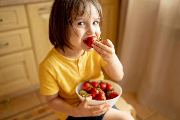 Smiling boy eating strawberry from bowl at home model released, Symbolfoto property released, ANAF01569