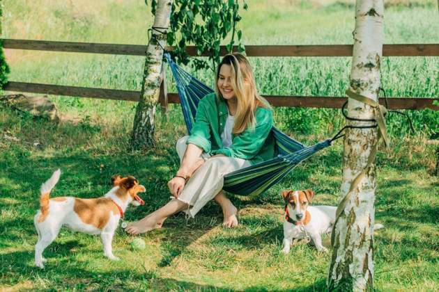IMAGO Creative: Sommer, Sommertage im Garten Smiling woman sitting on hammock with dogs model released, Symbolfoto property released, VSNF01119