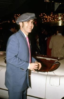British rocker Elton John wearing a grey suit and cap, smiling, holding a drink in front of a white car, at New York celebrity event, 1970s. Photo: Oscar Abolafia Everett Collection (eltonjohn001)OSAB001 J4533 PUBLICATIONXNOTxINxCANxCHNxFRAxITAxJPNxNORxPOLxRUSxESPxUKxUSA Copyright: xx OSAB001 J4533 OSAB001_J4533_H