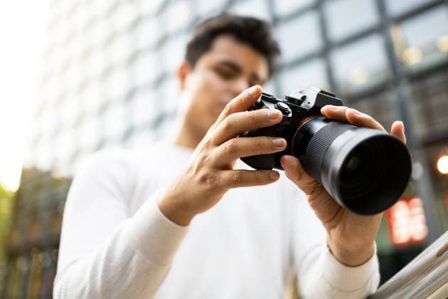 Blur Caucasian young man wearing white t-shirt viewing photos on camera while standing against blurred background in city Model Released DavidMunoz_ID15849_482530_016 Copyright: xDavidxMunozx