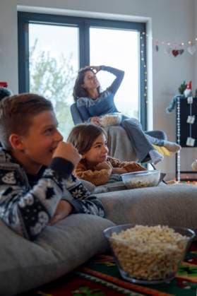 IMAGO Creative, Weihnachten, Tradition: Weihnachtsfilme sehen Siblings watching TV with mother and eating popcorn at home model released, Symbolfoto property released, IKF01088