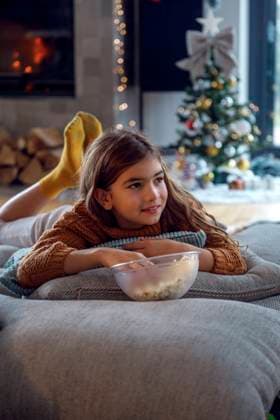 IMAGO Creative, Weihnachten, Tradition: Weihnachtsfilme sehen Girl having popcorn lying on pillows in living room model released, Symbolfoto property released, IKF01092