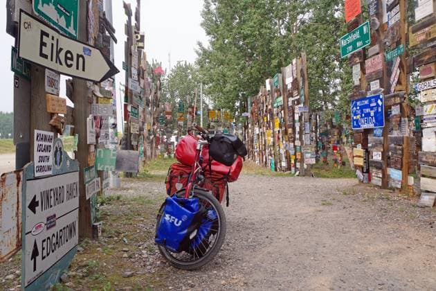 Verschiedene Verkehrs- und Ortschilder stehen einem mit Gepäck beladenem Fahrrad, Schilderwald, Abenteuerreise, Watson Lake, Yukon Territory, Kanada, Nordamerika Copyright: imageBROKER/ReinhardxPantke iblrpa09447488.jpg