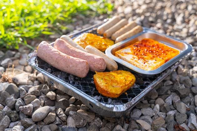 Bavaria, Germany - 2 September 2023: Vegetarian Grilling, Bratwurst Vegan and Vegetarian on a disposable grill on pebbles next to a meadow. Meat and sausage substitutes *** Vegetarisch Grillen, Bratwürste Vegan und Vegetarisch auf einem Einweggrill auf Kieselsteinen neben einer Wiese. Fleisch und Wurst Ersatzprodukte