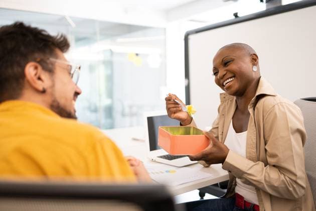 Happy black woman with a plate and spoon eating while sitting with a smiling man looking at each other under the office lights Model Released DavidMunoz_ID16062_488872_078 Copyright: xDavidxMunozx