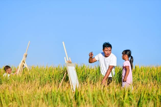 (230910) -- GUIDING, Sept. 10, 2023 -- Lu Chengwen (C) iinstructs as a student learns to paint from life amid terraced fields in Yanshan Township of Guiding County, southwest China s Guizhou Province, Sept. 6, 2023. Yanjiao teaching point is a micro primary school located at a flat area among mountains in southwest China s Guizhou. Lu Chengwen is the only teacher here with 28 preschool and 6 grade one students. In 2012, Lu, who had just graduated from the university, chose to teach at the remote Yanjiao teaching point. Preschool students, grown up from the mountainous village of the Miao ethnic group, could hardly speak Mandarin Chinese. In order to help his students learn Chinese characters and Mandarin Chinese, Lu taught them bilingu 