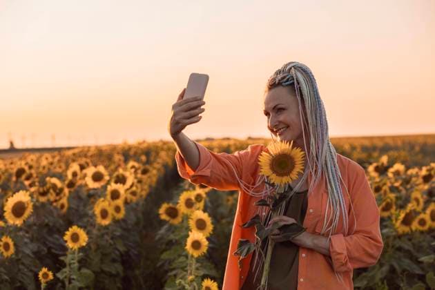 Smiling woman taking selfie through smart phone and holding sunflower in field model released, Symbolfoto property released, ADF00147