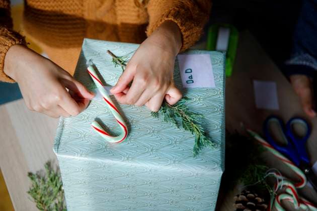 Girl sticking candy cane on gift box at home model released, Symbolfoto property released, IKF01155