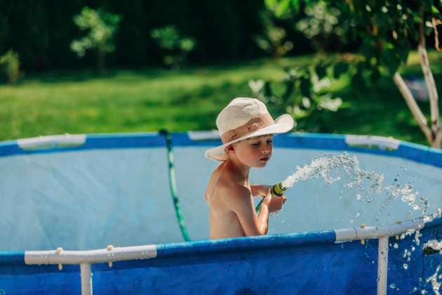 Boy wearing hat playing with water pipe in wading pool on sunny day model released, Symbolfoto, VSNF01330