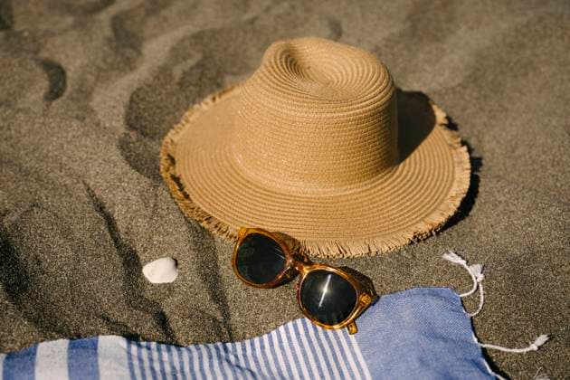 Sun hat next to sunglasses on sand at beach, YBF00201
