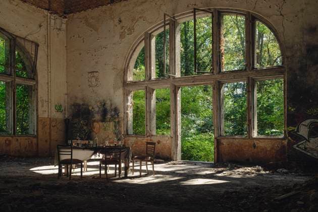 Symbolbild Beelitz Heilstätten Deutschland, Beelitz am 09.09.2023: In der Ruine des Speisesaals im Alpen-Haus stehen fünf alte Stühle und um einen alten Tisch mit Gläser und eine Flasche vor einem riesen Fenster. *** Symbolic image Beelitz Heilstätten Germany, Beelitz on 09 09 2023 In the ruin of the dining room in the Alpen Haus are five old chairs and around an old table with glasses and a bottle in front of a giant window