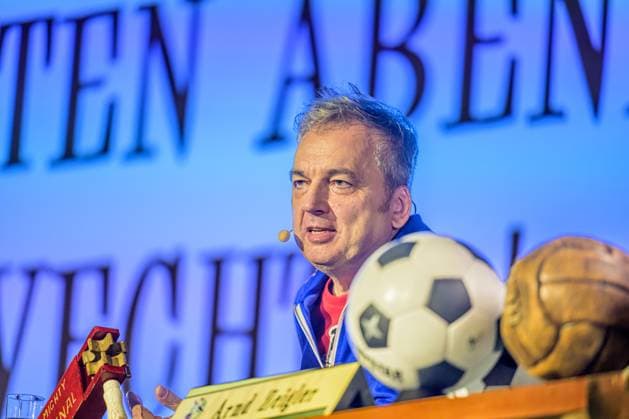 Zeiglers wunderbare Welt des Fußballs 27.09.2023, Uni Aula, Vechta, Zeiglers wunderbare Welt des Fußballs, Der Moderator strickt Fußballträume: Witzig, traurig, skurril und immer auch ein bisschen böse. Offen und unverblümt redet er in seinem Arbeitszimmer über Tragik, Tränen und Triumphe im Bild Arnd Zeigler (Moderator, ) an seinem Bühnenschreibtisch in der Aula der Uni Vechta vor ausverkauften Haus.