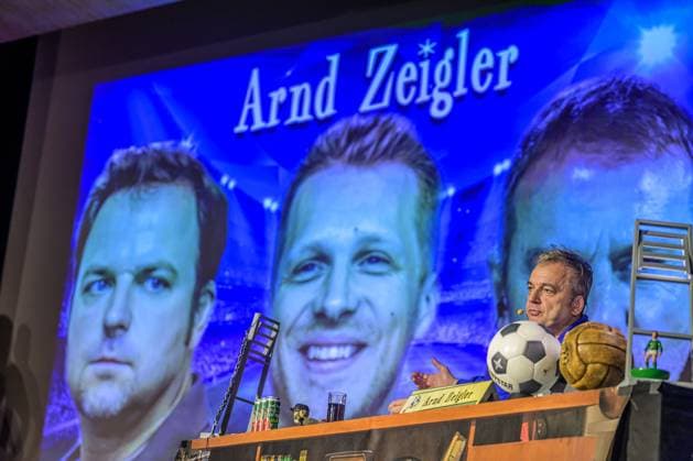 Zeiglers wunderbare Welt des Fußballs 27.09.2023, Uni Aula, Vechta, Zeiglers wunderbare Welt des Fußballs, Der Moderator strickt Fußballträume: Witzig, traurig, skurril und immer auch ein bisschen böse. Offen und unverblümt redet er in seinem Arbeitszimmer über Tragik, Tränen und Triumphe im Bild Arnd Zeigler (Moderator, ) an seinem Bühnenschreibtisch in der Aula der Uni Vechta vor ausverkauften Haus.