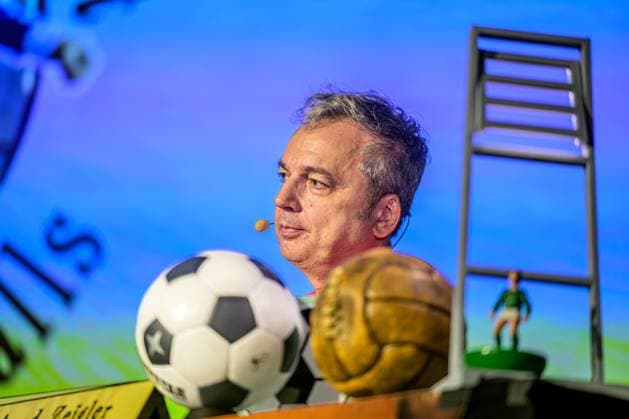 Zeiglers wunderbare Welt des Fußballs 27.09.2023, Uni Aula, Vechta, Zeiglers wunderbare Welt des Fußballs, Der Moderator strickt Fußballträume: Witzig, traurig, skurril und immer auch ein bisschen böse. Offen und unverblümt redet er in seinem Arbeitszimmer über Tragik, Tränen und Triumphe im Bild Arnd Zeigler (Moderator, ) an seinem Bühnenschreibtisch in der Aula der Uni Vechta vor ausverkauften Haus.