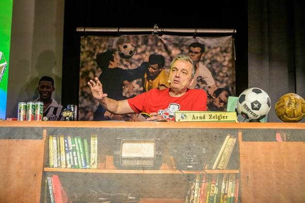 Entertainment Bilder des Tages Zeiglers wunderbare Welt des Fußballs 27.09.2023, Uni Aula, Vechta, Zeiglers wunderbare Welt des Fußballs, Der Moderator strickt Fußballträume: Witzig, traurig, skurril und immer auch ein bisschen böse. Offen und unverblümt redet er in seinem Arbeitszimmer über Tragik, Tränen und Triumphe im Bild Arnd Zeigler (Moderator, ) an seinem Bühnenschreibtisch in der Aula der Uni Vechta vor ausverkauften Haus.