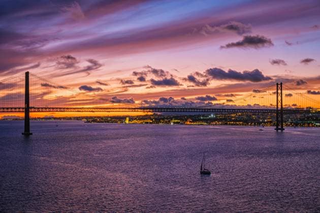 Blick auf die Brücke 25 de Abril, berühmtes touristisches Wahrzeichen von Lissabon, die Lisboa und Almada auf der Halbinsel Setubal verbindet, über den Fluss Tejo in der Abenddämmerung mit Booten. Lissabon, Portugal, Europa *** View at the Bridge 25 de Abril, Famous tourist Landmark from Lisbon, the Lisboa and Almada at the Peninsula Setubal connects, via the River Tejo in the Twilight with Boating Lisbon, Portugal, Europe Copyright: imageBROKER DmitryxRukhlenko ibxdmr09639931.jpg