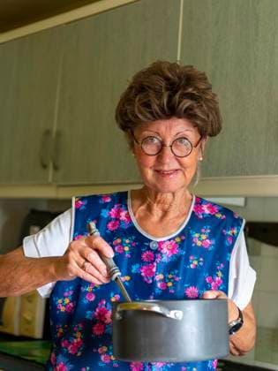 Oma mit alter Kittelschürze, Brille und Perücke in der Küche, hält Kochtopf und Kelle in Händen, Deutschland, Europa