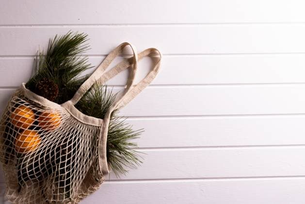Net bag with chrsitmas fir tree branches and oranges, copy space on white background. Christmas, decorations, tradition and celebration concept.