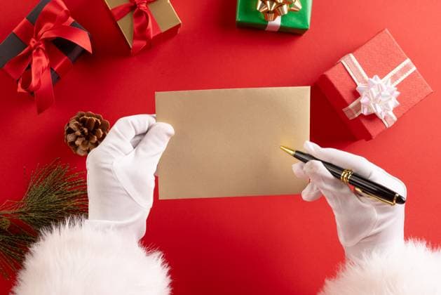 Santa claus holding envelope and pencil with copy space and christmas presents on red background. Santa claus, christmas, tradition and celebration concept.