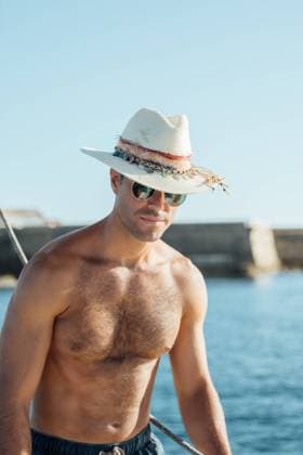 Young fit shirtless man in swimming shorts and hat standing on sailboat enjoying summer vacation against sea and cloudless blue sky Model Released AlvaroMontero_ID16707_510355_005 Copyright: xAlvaroxMonterox RECORD DATE NOT STATED