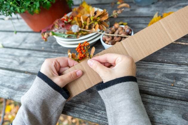 7 October 2023: Children s fun with autumn leaves: creative crafts at home. Child glues bushes and pine cones to a cardboard box to make an autumn crown *** Kinderspaß mit Herbstlaub: Kreatives Basteln zu Hause. Kind Klebt Sträucher und Tannenzapfen an einen Pappkarton um eine herbstliche Krone zu bauen