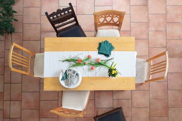 Preparation for a table setting with white plates and bowls, cutlery, green napkins and some tulip flowers, different wooden chairs around on a tiled terracotta floor, high angle view from above Preparation for a table setting with white plates and bowls, cutlery, green napkins and some tulip flowers, different wooden chairs around on a tiled terracotta floor, high angle view from above, selected focus Copyright: xZoonar.com MARENxWINTERx 20533346